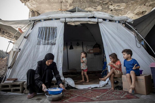 Mulher prepara alimento diante de uma barraca com crianças no campo de Al Saraya, em Gaza.
