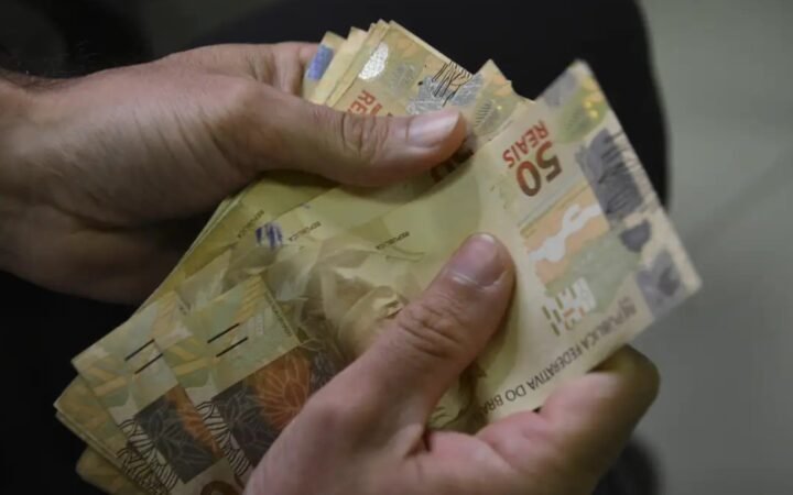 Mãos contam cédulas de cinquenta reais.